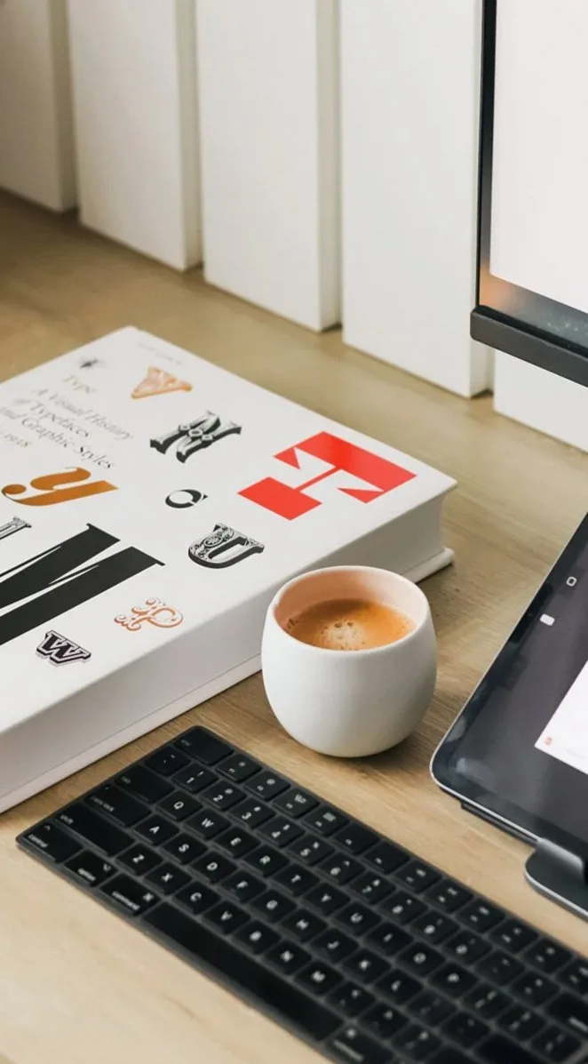 書体の本とコーヒーカップ、キーボードが置かれた木のデスク